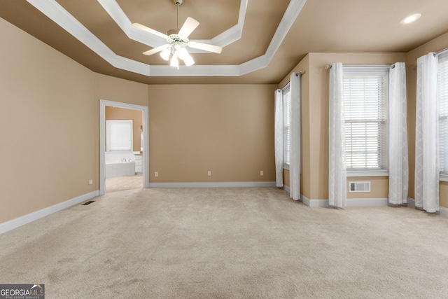 empty room with visible vents, crown molding, a ceiling fan, a raised ceiling, and carpet flooring