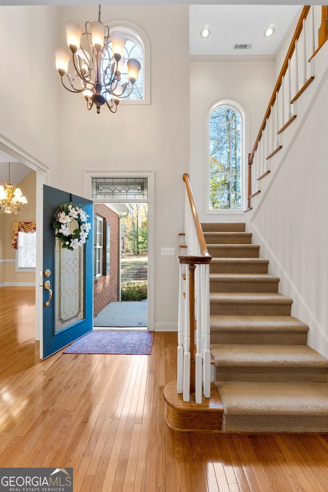 foyer featuring a notable chandelier, light wood finished floors, stairs, baseboards, and visible vents