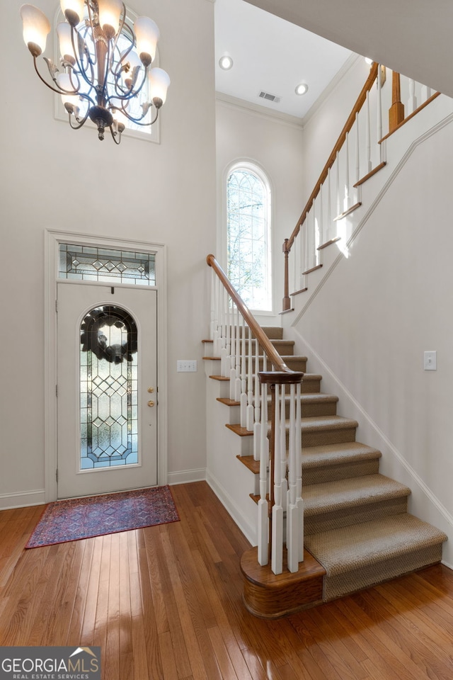 foyer entrance featuring visible vents, wood-type flooring, baseboards, stairway, and a notable chandelier