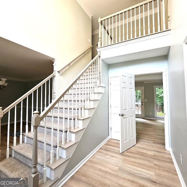 stairs featuring crown molding, baseboards, a high ceiling, and wood finished floors