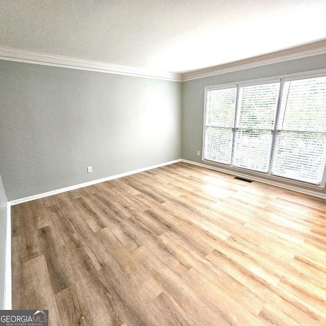 empty room with baseboards, visible vents, ornamental molding, and wood finished floors