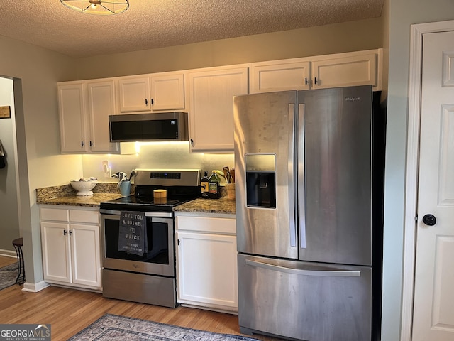 kitchen with dark stone counters, stainless steel appliances, light wood-type flooring, and white cabinetry