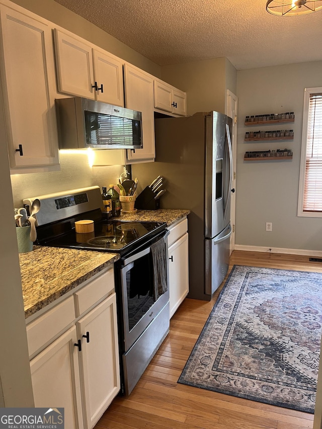 kitchen featuring a textured ceiling, light stone counters, light wood-style floors, stainless steel appliances, and white cabinetry