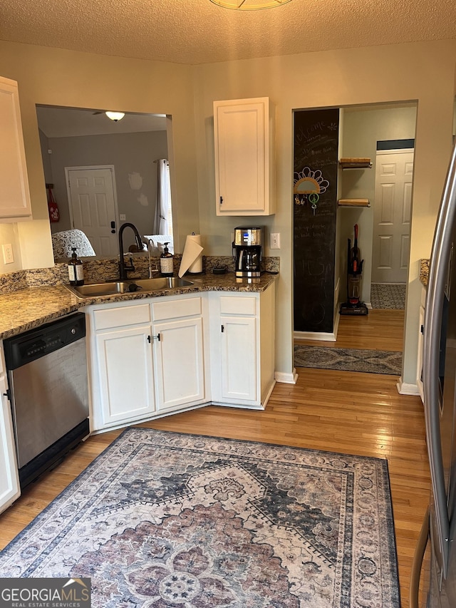 kitchen featuring stainless steel dishwasher, a sink, light wood-style flooring, and white cabinets