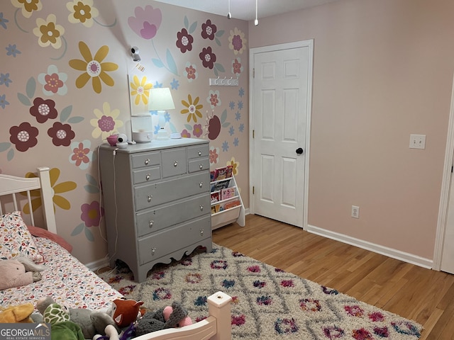 bedroom featuring baseboards, wallpapered walls, and light wood-style floors