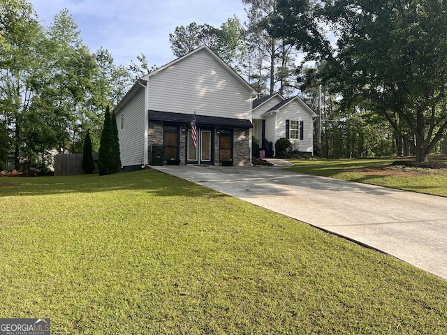 traditional-style home with a front yard, fence, driveway, and stone siding