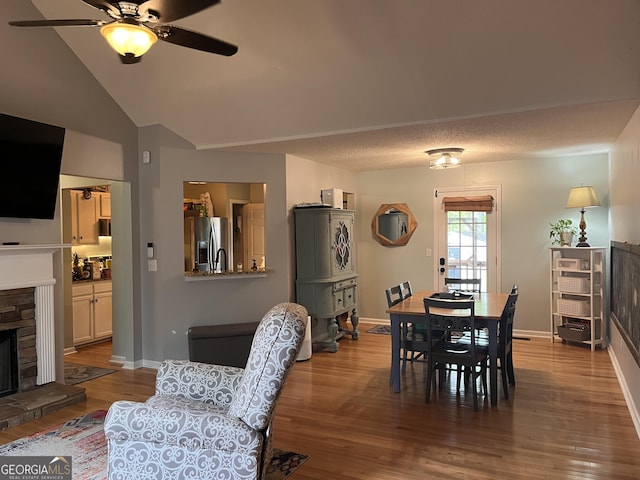 dining space with a stone fireplace, a ceiling fan, baseboards, and wood finished floors