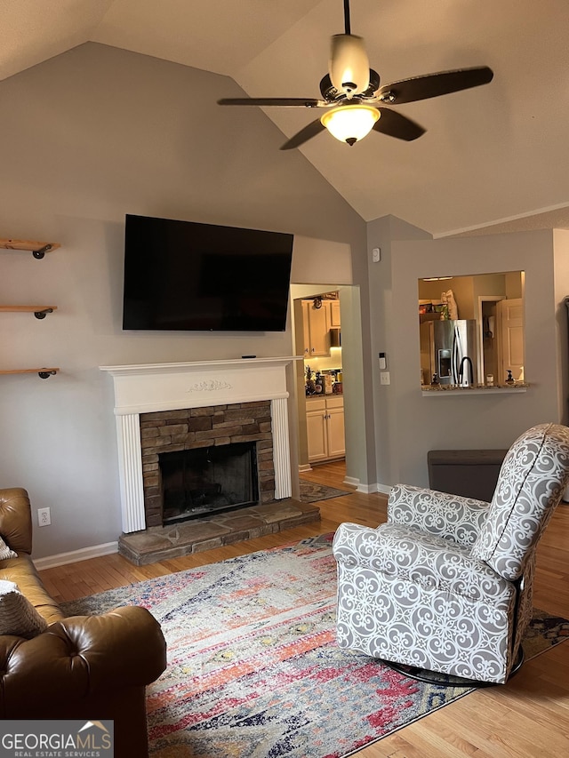 living area featuring wood finished floors, lofted ceiling, a fireplace, baseboards, and ceiling fan