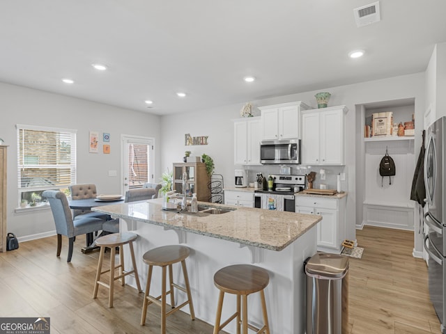 kitchen with a sink, a kitchen breakfast bar, stainless steel appliances, light wood-type flooring, and visible vents