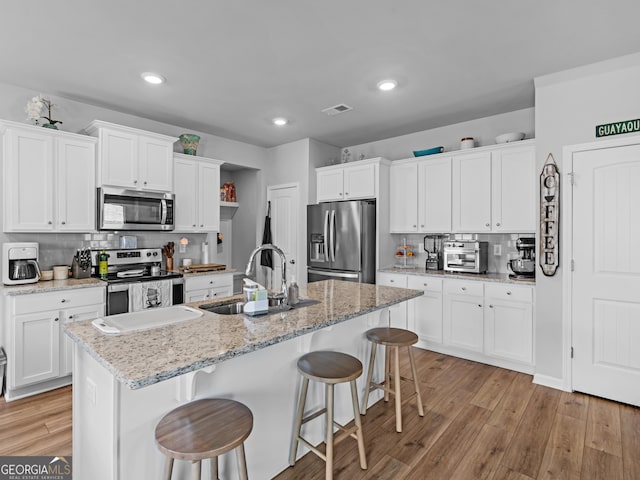kitchen with light wood-style floors, a breakfast bar area, white cabinets, a sink, and stainless steel appliances