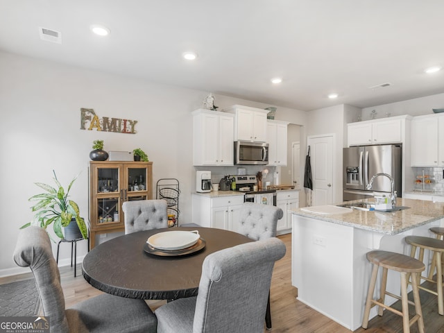 kitchen with visible vents, a breakfast bar area, light wood-type flooring, white cabinetry, and stainless steel appliances