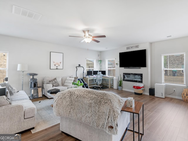 living area featuring ceiling fan, visible vents, a healthy amount of sunlight, and wood finished floors