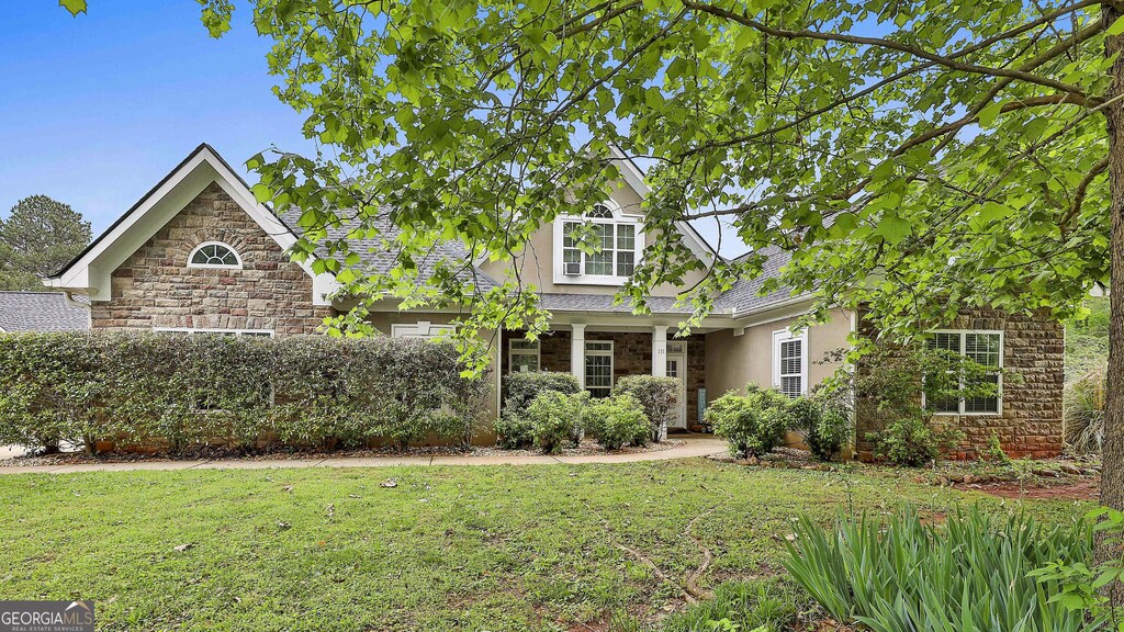 view of front facade featuring stucco siding, a front lawn, and stone siding