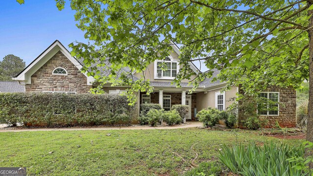 view of front facade featuring stucco siding, a front lawn, and stone siding
