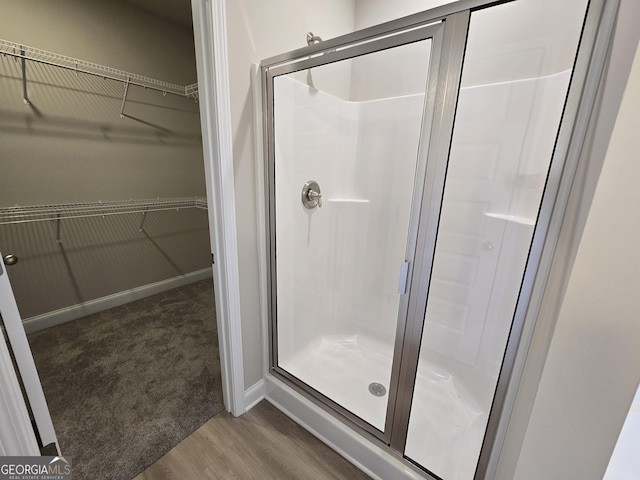 full bath with wood finished floors, baseboards, a walk in closet, and a stall shower
