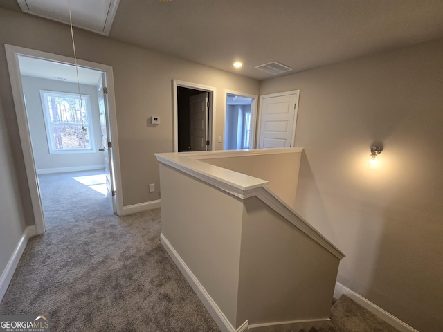 hallway with attic access, visible vents, baseboards, an upstairs landing, and carpet flooring