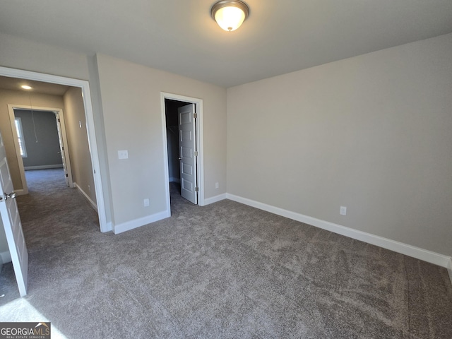 unfurnished bedroom featuring a walk in closet, baseboards, and dark carpet