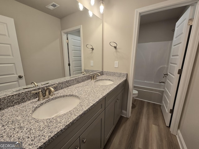 bathroom with double vanity, toilet, a sink, and wood finished floors