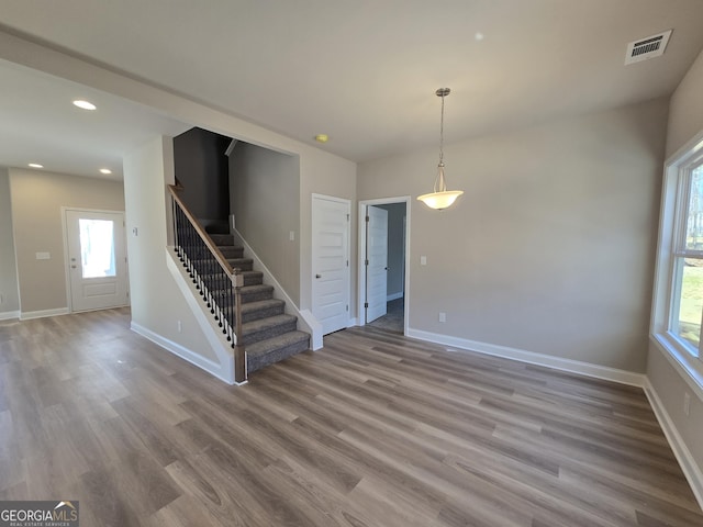 unfurnished living room featuring baseboards, stairs, wood finished floors, and visible vents