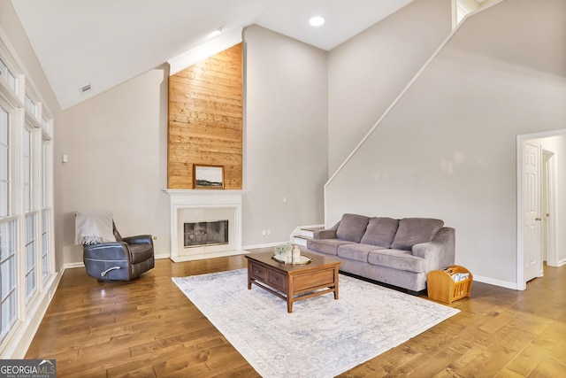 living area with baseboards, a glass covered fireplace, wood finished floors, and high vaulted ceiling