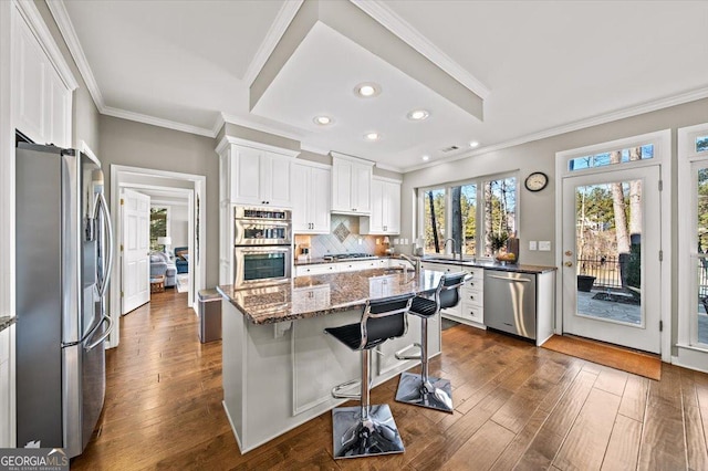 kitchen with dark wood finished floors, dark stone countertops, stainless steel appliances, decorative backsplash, and ornamental molding