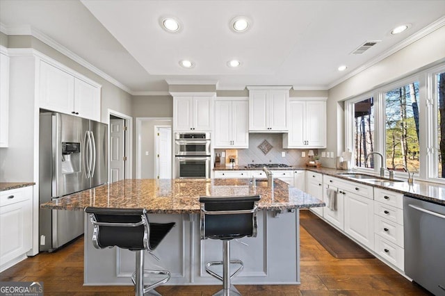 kitchen with a sink, appliances with stainless steel finishes, ornamental molding, and stone counters