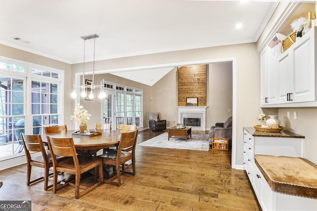 dining space with visible vents, vaulted ceiling, wood-type flooring, a glass covered fireplace, and ornamental molding