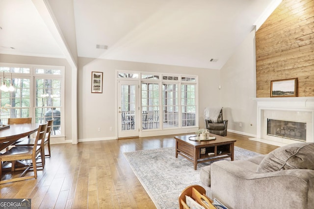 living area featuring high vaulted ceiling, visible vents, plenty of natural light, and a glass covered fireplace