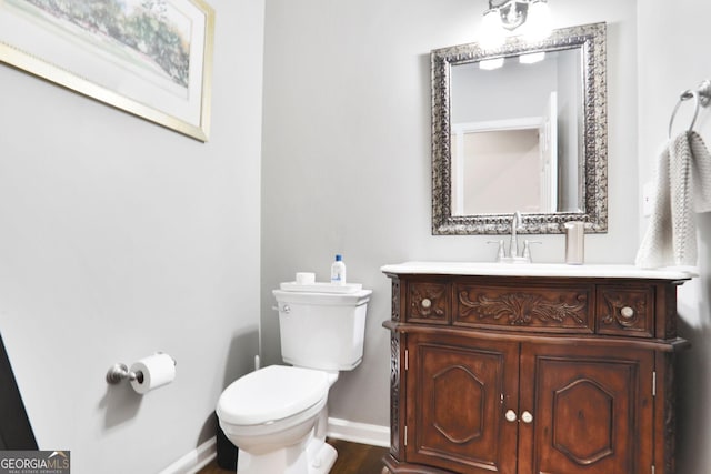 half bathroom with toilet, baseboards, wood finished floors, and vanity