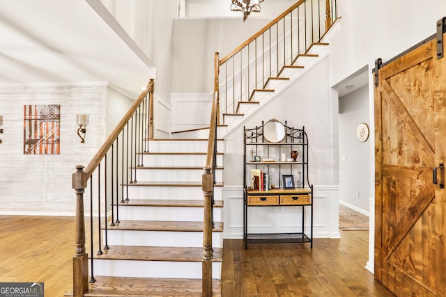 staircase featuring baseboards, a barn door, a towering ceiling, and hardwood / wood-style floors