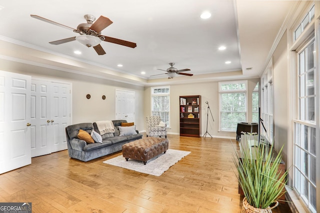 living room featuring crown molding, light wood-style floors, baseboards, ceiling fan, and a tray ceiling