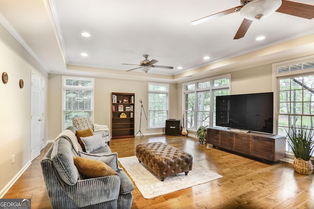 living room with a tray ceiling, plenty of natural light, ornamental molding, and a ceiling fan