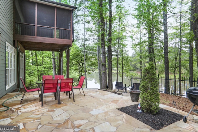 view of patio with outdoor dining area, a water view, fence, and a sunroom