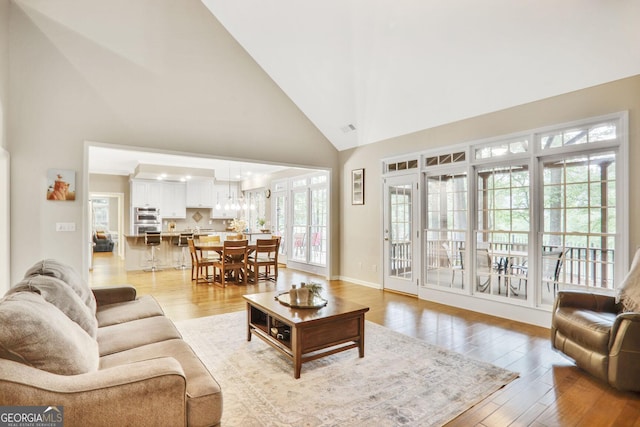 living area with visible vents, baseboards, high vaulted ceiling, a chandelier, and light wood-style flooring