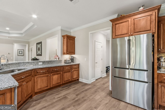 kitchen featuring freestanding refrigerator, brown cabinets, light stone counters, a sink, and light wood finished floors