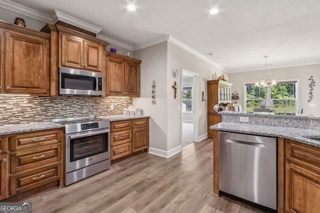 kitchen with brown cabinetry, decorative backsplash, a chandelier, light wood-style flooring, and stainless steel appliances