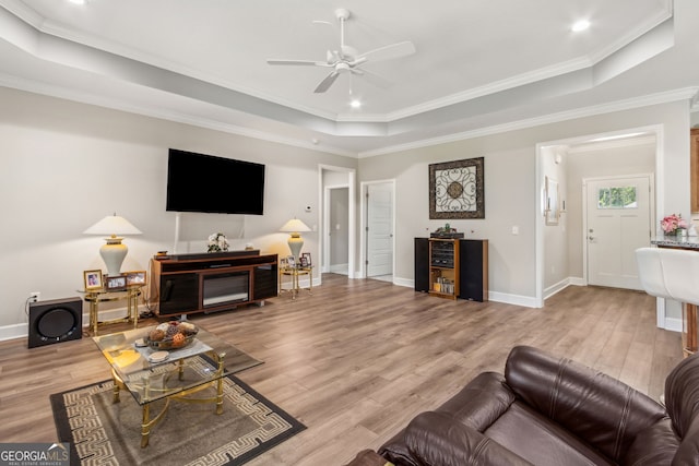 living room featuring ceiling fan, ornamental molding, a tray ceiling, and wood finished floors