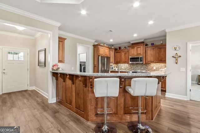 kitchen with a kitchen breakfast bar, brown cabinets, baseboards, stainless steel appliances, and light wood-style flooring