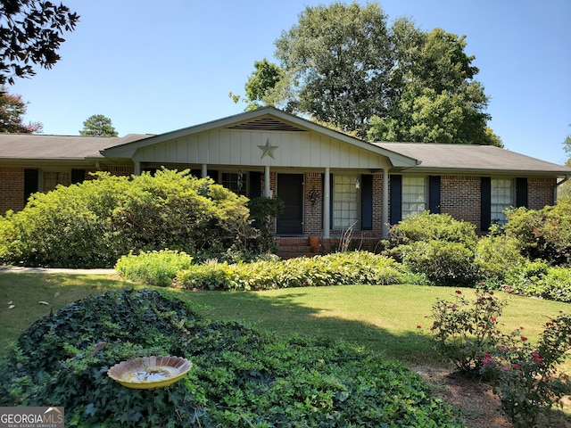ranch-style home featuring covered porch, brick siding, and a front lawn