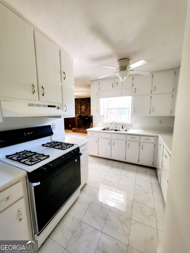 kitchen with marble finish floor, ceiling fan, under cabinet range hood, a sink, and gas stove