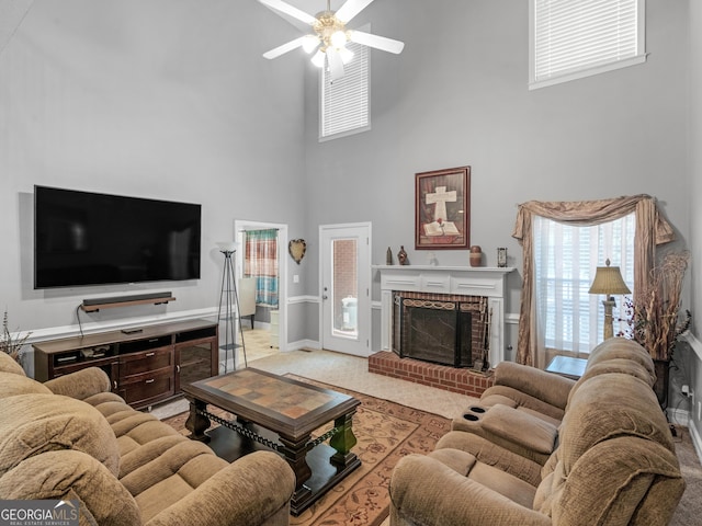 living area with a brick fireplace, baseboards, ceiling fan, a high ceiling, and light colored carpet