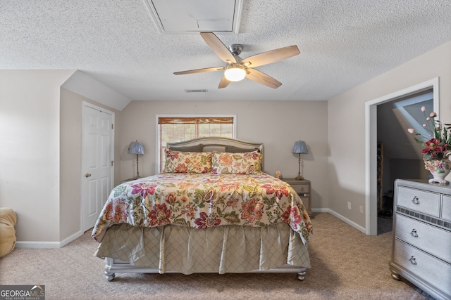 carpeted bedroom with a textured ceiling, attic access, a ceiling fan, baseboards, and visible vents