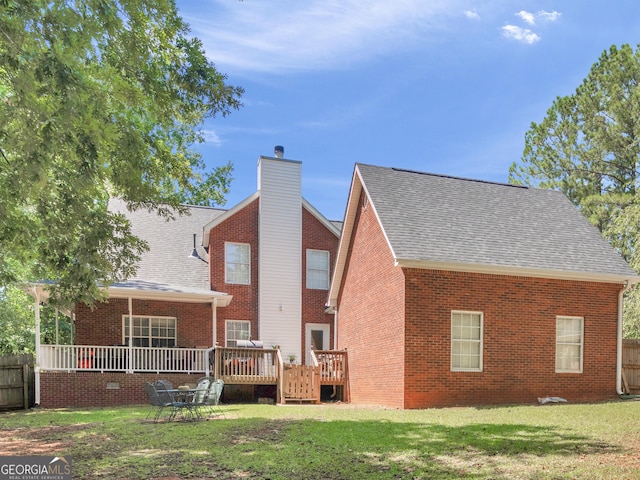 rear view of property featuring a deck, roof with shingles, a chimney, brick siding, and a lawn