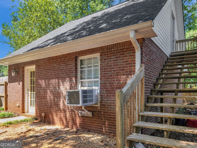 view of home's exterior with stairway, brick siding, cooling unit, and a shingled roof