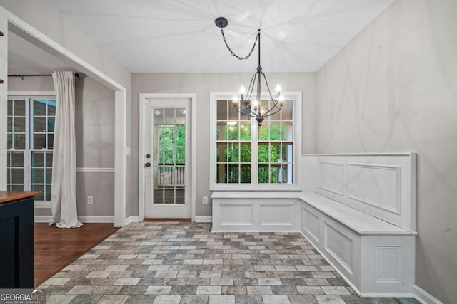 unfurnished dining area with an inviting chandelier, baseboards, wainscoting, and a decorative wall