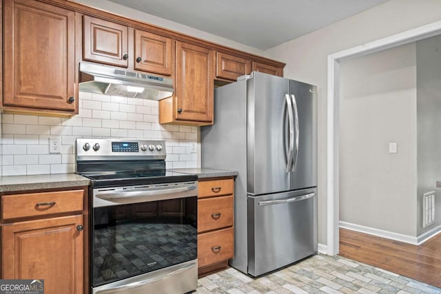 kitchen with appliances with stainless steel finishes, tasteful backsplash, brown cabinets, baseboards, and under cabinet range hood