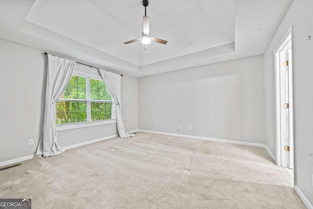 carpeted spare room featuring a ceiling fan, a tray ceiling, visible vents, and baseboards