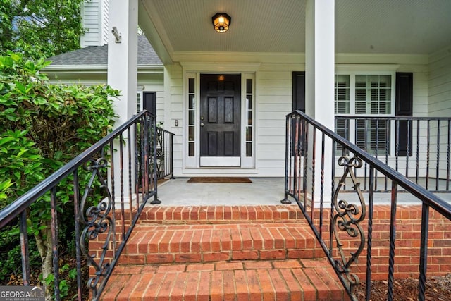 view of exterior entry with roof with shingles and a porch