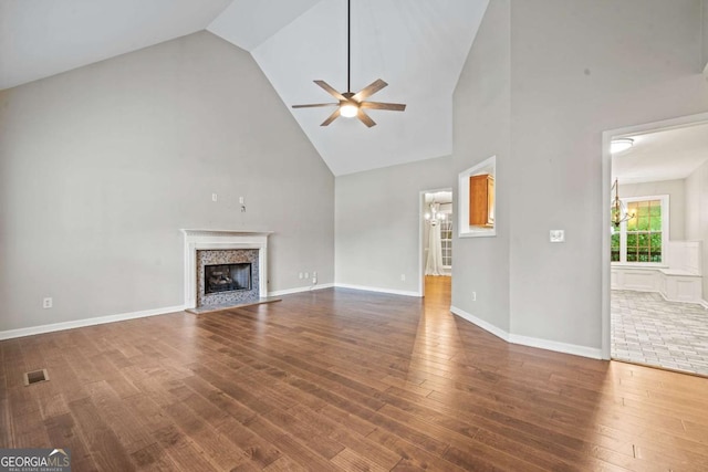 unfurnished living room with visible vents, wood finished floors, a fireplace, high vaulted ceiling, and ceiling fan with notable chandelier