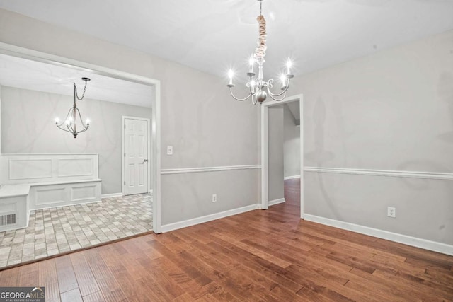 unfurnished dining area featuring an inviting chandelier, baseboards, wood finished floors, and visible vents